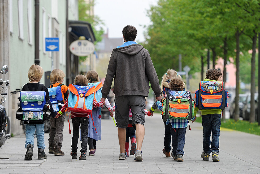 Bus mit Füßen: Kindergruppe in Begleitung eines Erwachsenen auf dem Schulweg